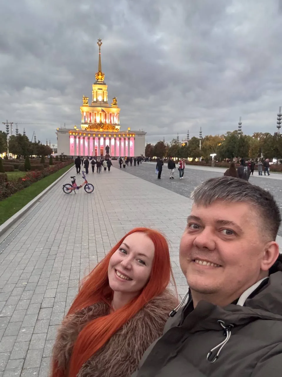Станислав Кириченко с женой на аллее ВДНХ, вдали подсвеченный павильон